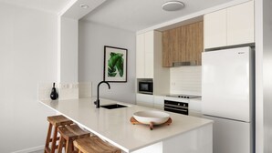 Una cucina moderna con mobili bianchi, un rubinetto nero, un forno a microonde, un piano cottura e un frigorifero. C'è uno sgabello di legno al bancone e un quadro appeso al muro.