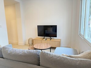 Een moderne woonkamer met een flatscreen televisie op een houten dressoir, een ronde salontafel en een grijze bank.