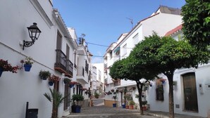 Una estrecha calle adoquinada flanqueada por edificios blancos, algunos con balcones y plantas en macetas.