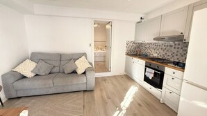 Cocina moderna con armarios blancos, sofá gris y salpicadero de azulejos.