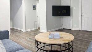 Een moderne woonkamer met een ronde salontafel, een flatscreen televisie aan de wand en een deur naar een andere kamer.