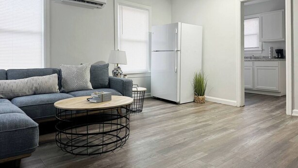 Een moderne woonkamer met een grijze bank, een ronde salontafel en een witte koelkast.