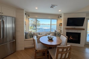 A modern kitchen with a built-in stove, a large window overlooking a lake, and a cozy seating area with a round table and chairs. - Unique Waterfront Luxury Home - Coastal Entertaining at it's Finest (Scituate)