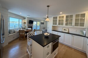 A modern kitchen with white cabinetry, a black countertop island, and a view of the outdoors. - Unique Waterfront Luxury Home - Coastal Entertaining at it's Finest (Scituate)
