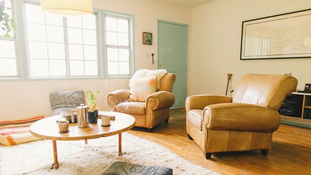 A living room with two leather armchairs, a round wooden coffee table, a white shag rug, and a large window with a view of the outside. - Classic Venice Beach Bungalow (Los Angeles)