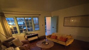 A living room with a sofa, armchair, and a coffee table. There is a window with curtains and a door leading outside. - Classic Venice Beach Bungalow (Los Angeles)