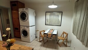 A compact kitchen with a washing machine, a dining table with two chairs, and a window with a cityscape view. - Classic Venice Beach Bungalow (Los Angeles)
