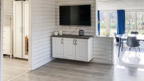 A modern room with a white cabinet, a flat-screen TV, and a dining area with a table and chairs.