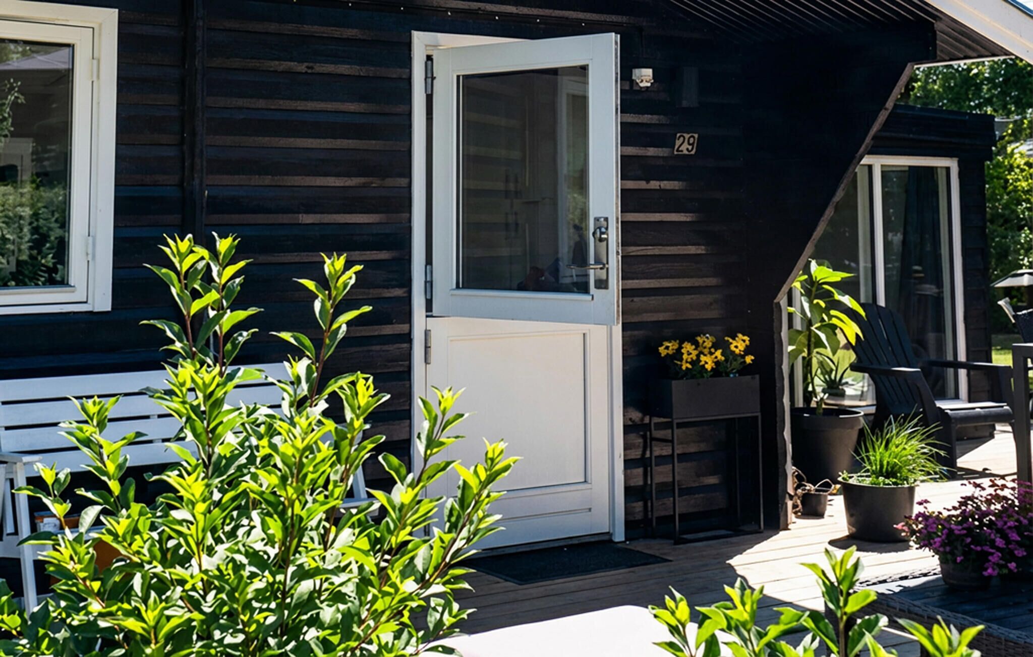 A wooden house with a white door, a small porch with potted plants, and a number '29' on the wall.
