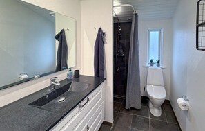 Un baño con lavamanos negro, espejo, inodoro, ducha y ventana con plantas.