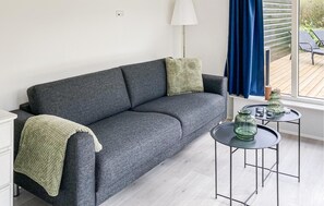Een grijze bank met een groene plaid, een klein rond tafeltje met kaarsen, en een raam met blauwe gordijnen.
