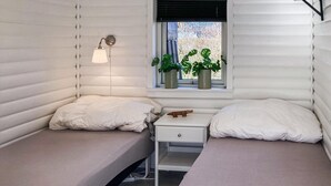 A compact, single-room cabin with two bunk beds, a small bedside table, and a window with potted plants.