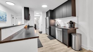 A modern kitchen with dark cabinetry, a central island, stainless steel appliances, and a minimalist design.