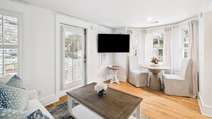En stue med sofa, sofabord med vase, fjernsyn monteret på væggen, samt spiseområde med bord og stole.