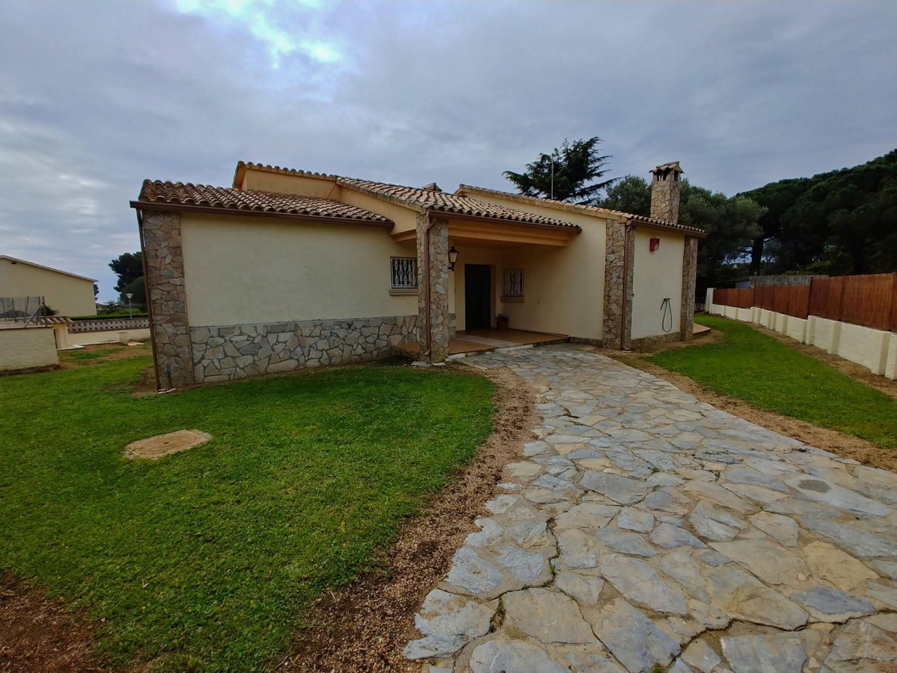 Une maison avec un chemin de pierre menant à l’entrée, entourée d’une pelouse bien entretenue et d’une clôture en bois.
