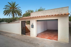 A small building with a garage, a staircase leading to the entrance, and a palm tree in the background.