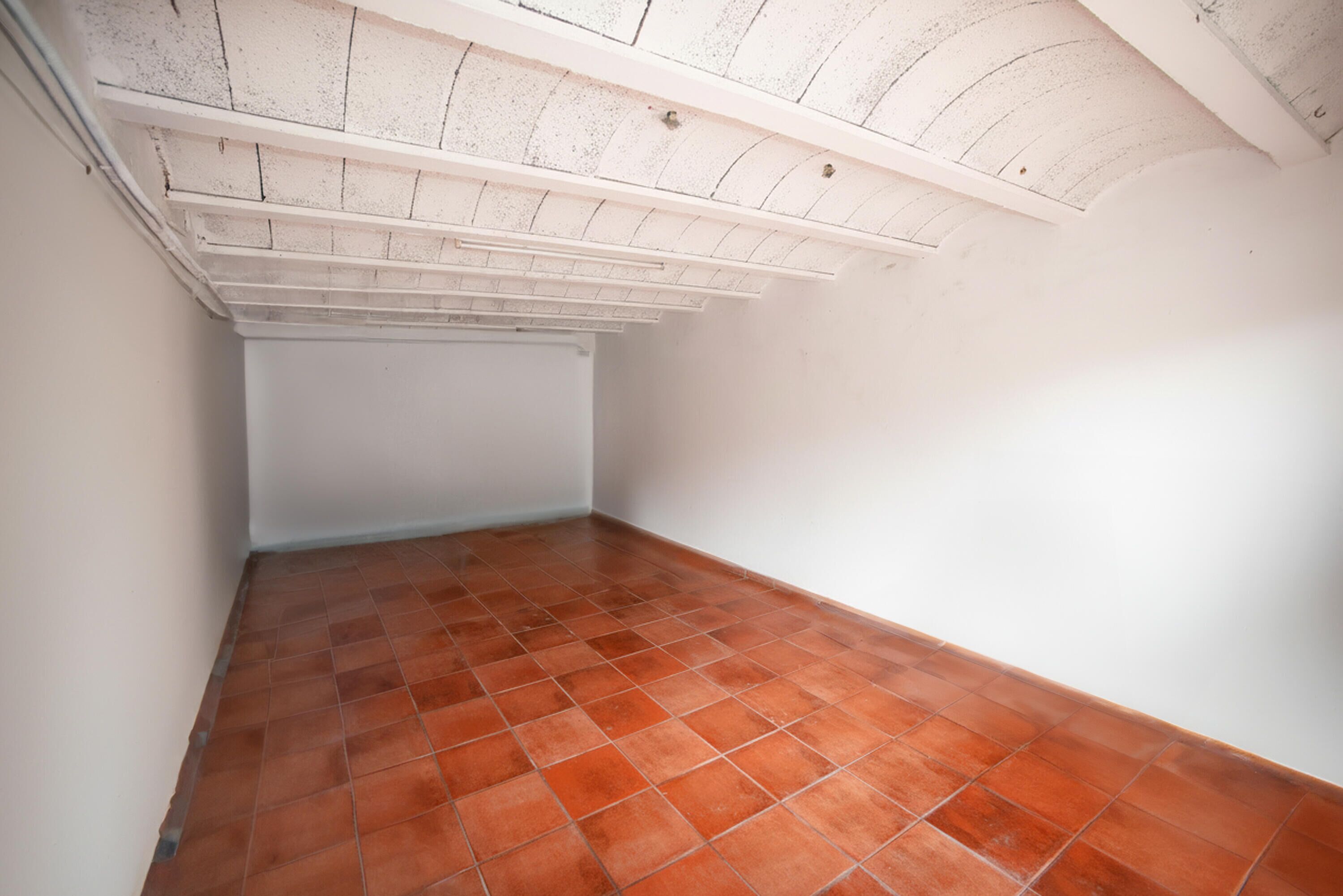 A room with a sloped ceiling, white walls, and terracotta floor tiles.