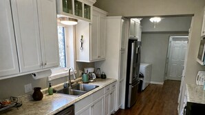 Une cuisine avec des meubles blancs, un lave-vaisselle, un réfrigérateur et un ventilateur de plafond.