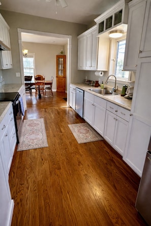 A kitchen with wooden floors, white cabinets, and a dining area with a wooden table and chairs.