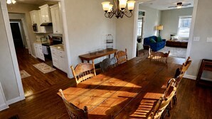 Un vaste espace dédié à la salle à manger, avec une grande table et des chaises en bois, un lustre, et une vue sur la cuisine et le salon.