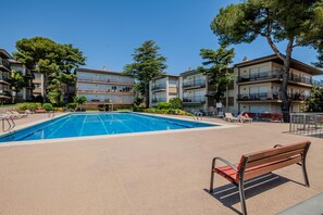 Ein Schwimmbecken mit Liegestühlen und einer Sitzbank, umgeben von mehrstöckigen Gebäuden mit Balkonen.
