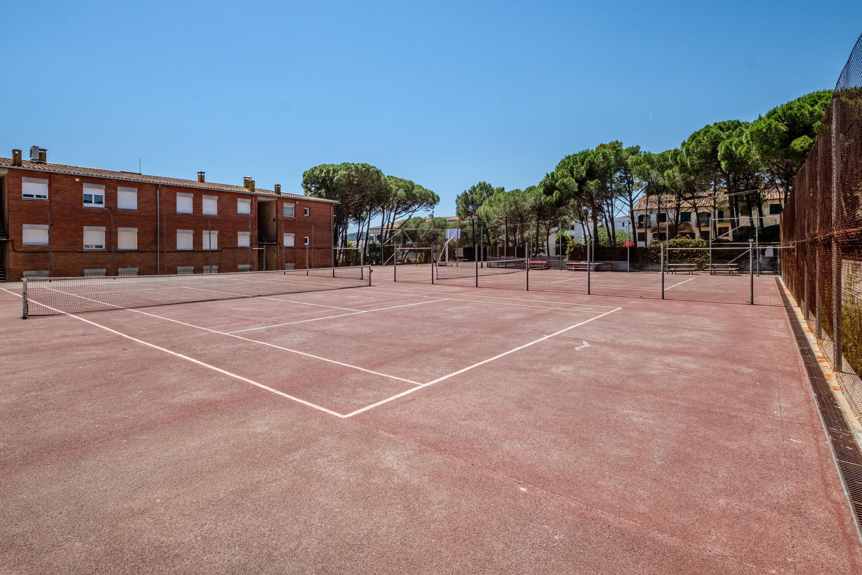 Un court de tennis en plein air, doté d’un filet, entouré de bâtiments et d’arbres.