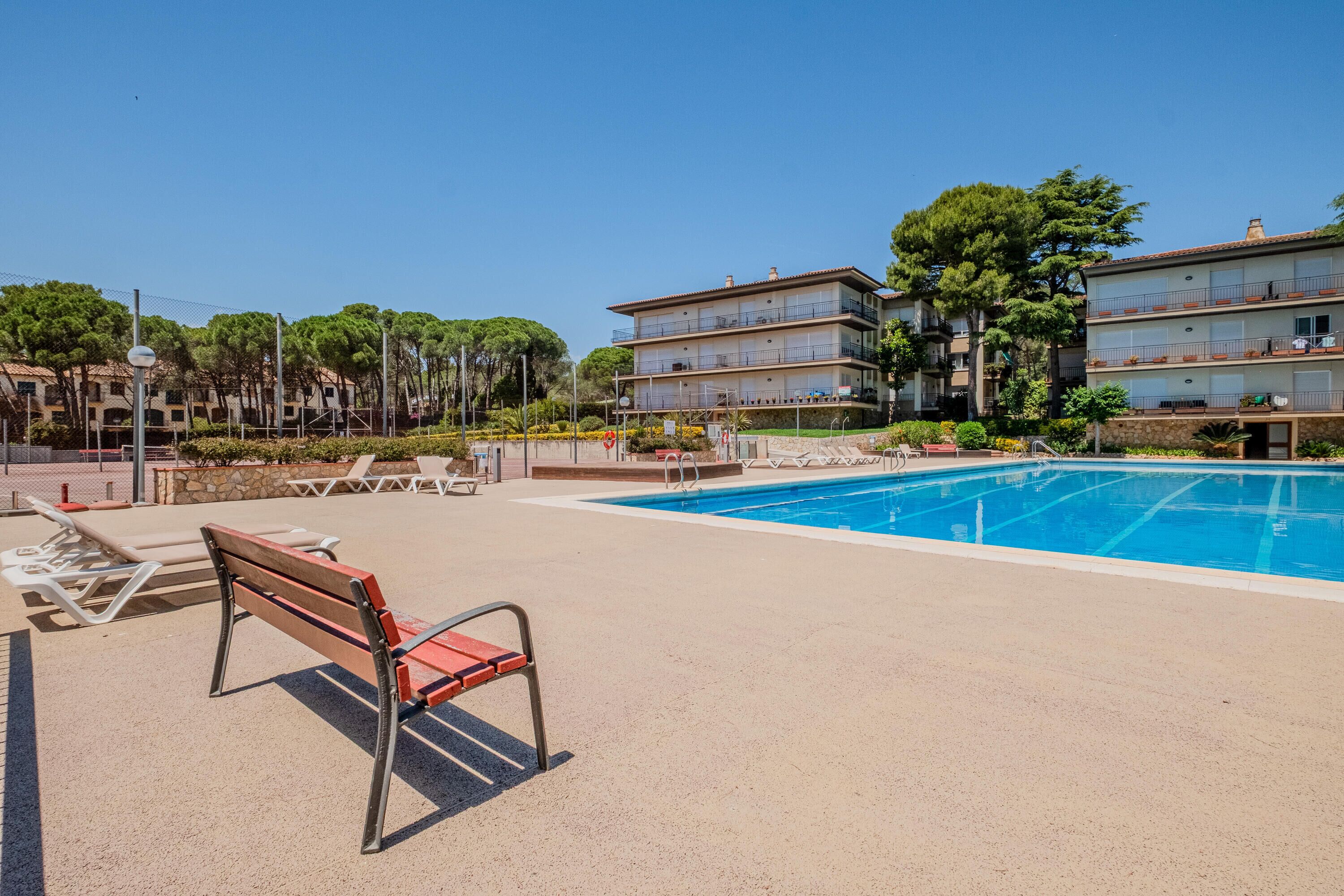 Área de piscina com espreguiçadeiras e um banco, cercada por edifícios com várias andares e varandas.