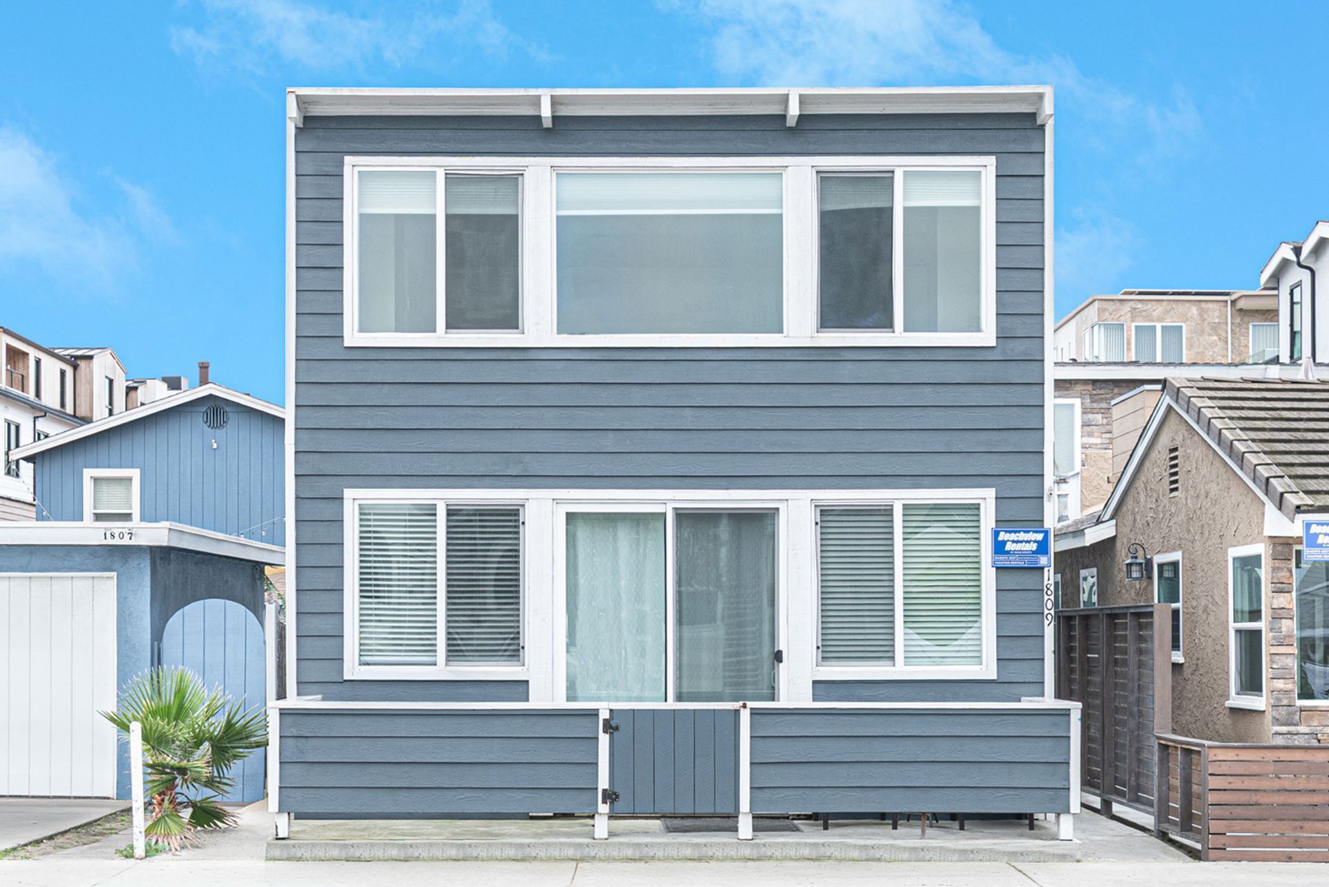 A two-story residential building with a flat roof, large windows, and a front porch.