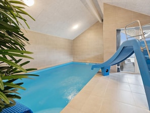 An indoor swimming pool with a blue slide, beige tiled walls, and a metal ladder. - 5 Star Holiday Home in Bogense (Bogense)