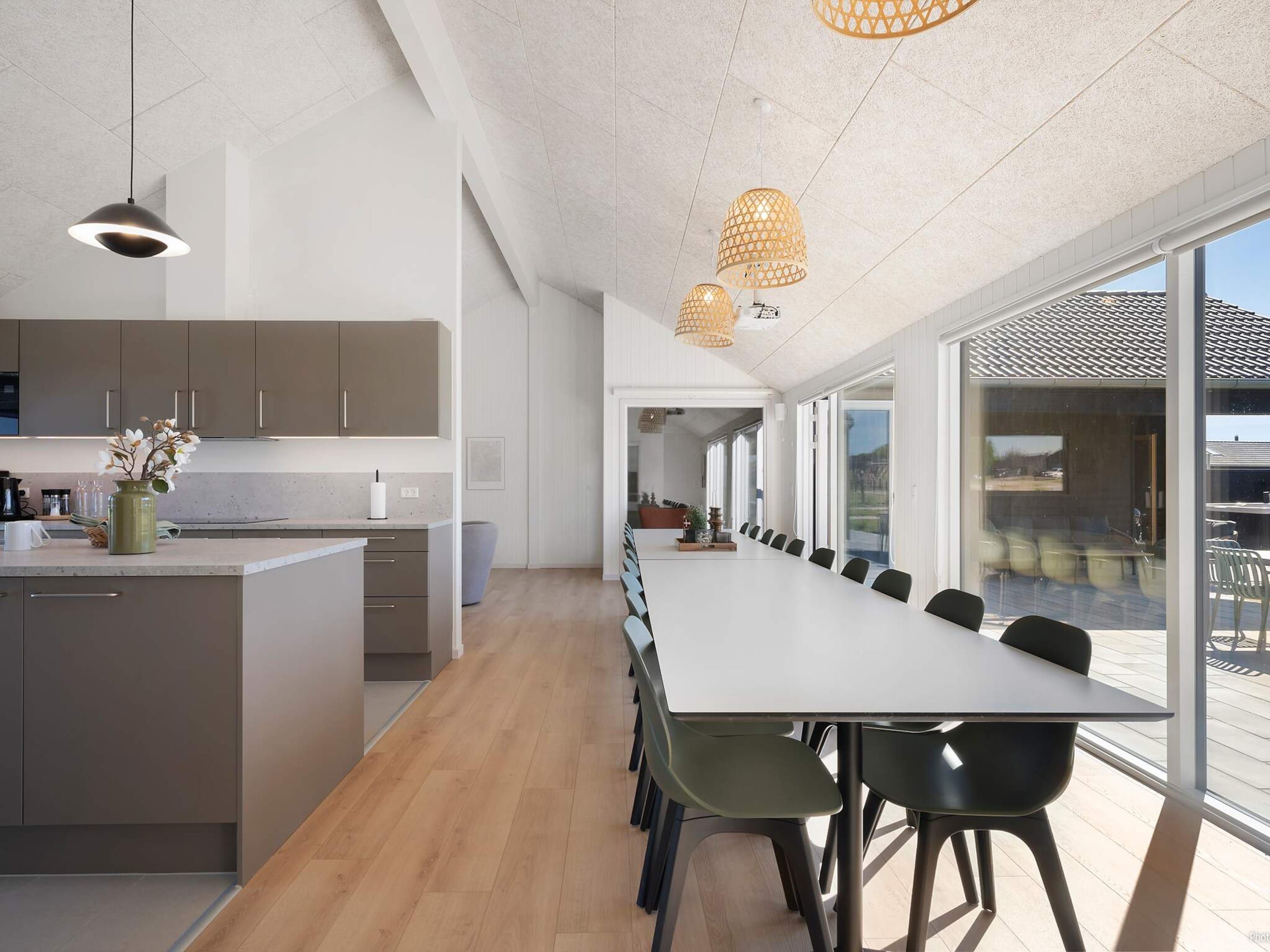 A modern kitchen with a long island, a dining area with a large table and chairs, and large windows providing a view of the outdoors.