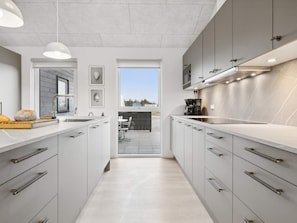 A modern kitchen with white cabinetry, a built-in oven, and a coffee machine. - 5 Star Holiday Home in Bogense (Bogense)