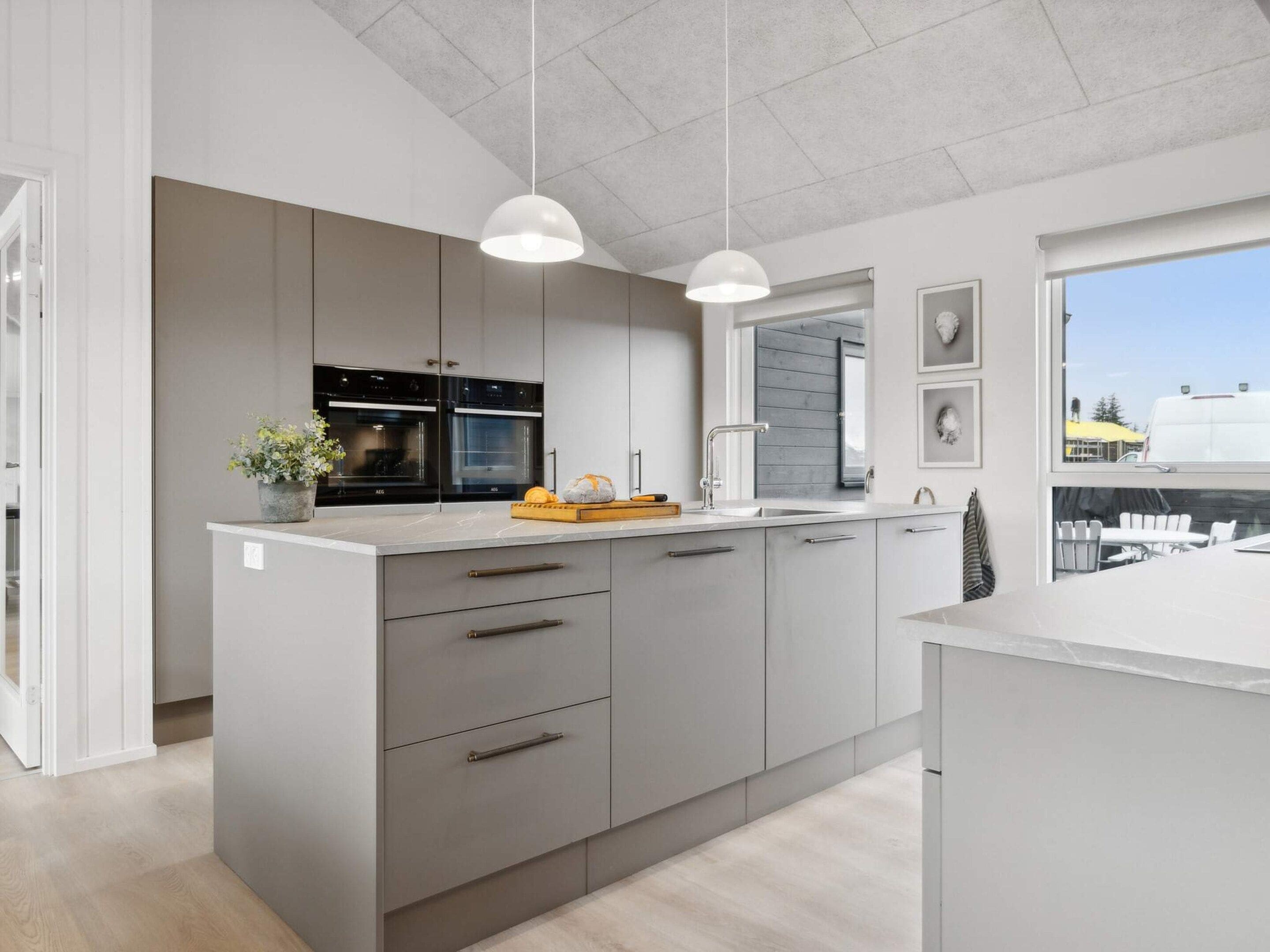 Een moderne keuken met een centraal eiland, inbouwapparatuur en hangende verlichting.