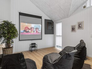 Quarto com uma tela grande, planta, cadeiras de poltrona e quadros nas paredes.