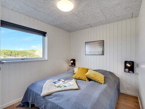 A bedroom with a bed, a window, a wall-mounted picture, and two wall sconces. - 5 Star Holiday Home in Bogense (Bogense)