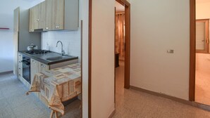 Eine Küche mit Schränken, einem Herd und einem Spülbecken. Im Vordergrund steht ein Tisch mit einer Tischdecke.