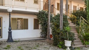Ein Gebäude mit weißer Fassade, einer Treppe, die zu einem Balkon führt, und einem Kieshof mit Laterne und Pflanzen in Töpfen.