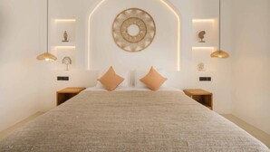 Een moderne slaapkamer met een groot bed, twee nachtkastjes, een rond plafondlamp aan de muur en twee hangende pendantlampen.