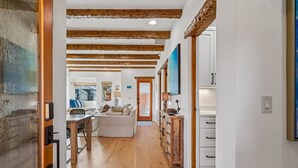 Un pasillo con vigas de madera, un comedor con mesa y sillas, un sofá y un aparador con cajones.
