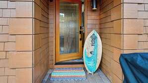 Una puerta de madera con un panel de vidrio, una tabla de surf apoyada en la pared y un tapete colorido en el suelo.