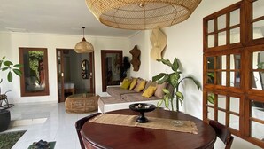 Un amplio salón con una gran mesa de comedor de madera, una lámpara de techo tejida y vistas al exterior a través de un ventanal.