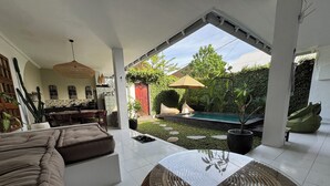 Una sala de estar moderna con un sofá grande, una mesa de centro de vidrio y vistas a una piscina y jardín.