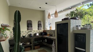 Cocina compacta con refrigerador, pileta y cafetera. Se observan baldosas decorativas y una planta de cactus.