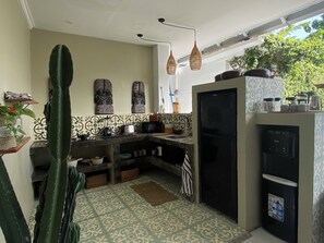 Eine kleine Küche mit Kühlschrank, Spüle und Kaffeemaschine. Dekorative Wandfliesen und eine Kakteenpflanze sind ebenfalls vorhanden.