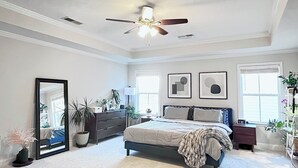 A bedroom with a bed, dresser, mirror, ceiling fan, and two windows. - New-built Modern home for 2026 Masters rental (Grovetown)