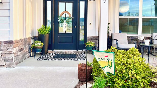 A front door with a dark color, a number sign, a porch with chairs, and a flag. - New-built Modern home for 2026 Masters rental (Grovetown)