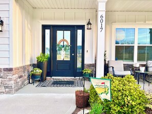 A front door with a dark color, a number sign, a porch with chairs, and a flag. - New-built Modern home for 2026 Masters rental (Grovetown)