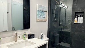 Een moderne badkamer met een wastafel met twee kommen, een toilet, een douchecabine van glas en een marmeren spatwand.