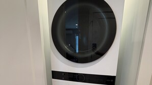 Een witte LG ThinQ wasmachine met een voorlaadontwerp, geplaatst in een hoek van een kamer met een witte deur en houten vloer.