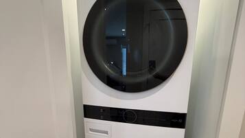 Een witte LG ThinQ wasmachine met een voorlaadontwerp, geplaatst in een hoek van een kamer met een witte deur en houten vloer.
