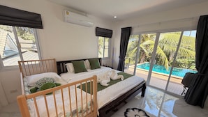 A bedroom with a large bed, a wooden crib, a pool view, and a modern air conditioning unit. - Quiet family-friendly villa in the city center (Chang Wat Surat Thani)